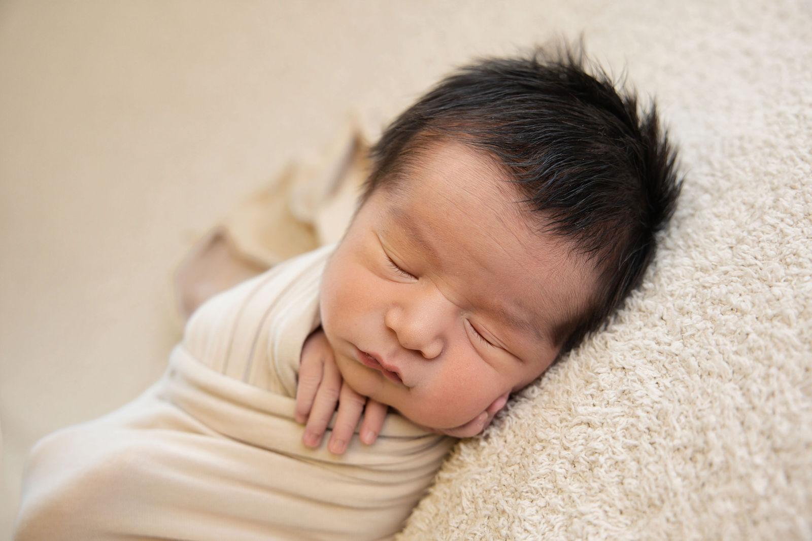 Close-up portrait of a sleeping newborn wrapped in soft cream fabric during a studio newborn session