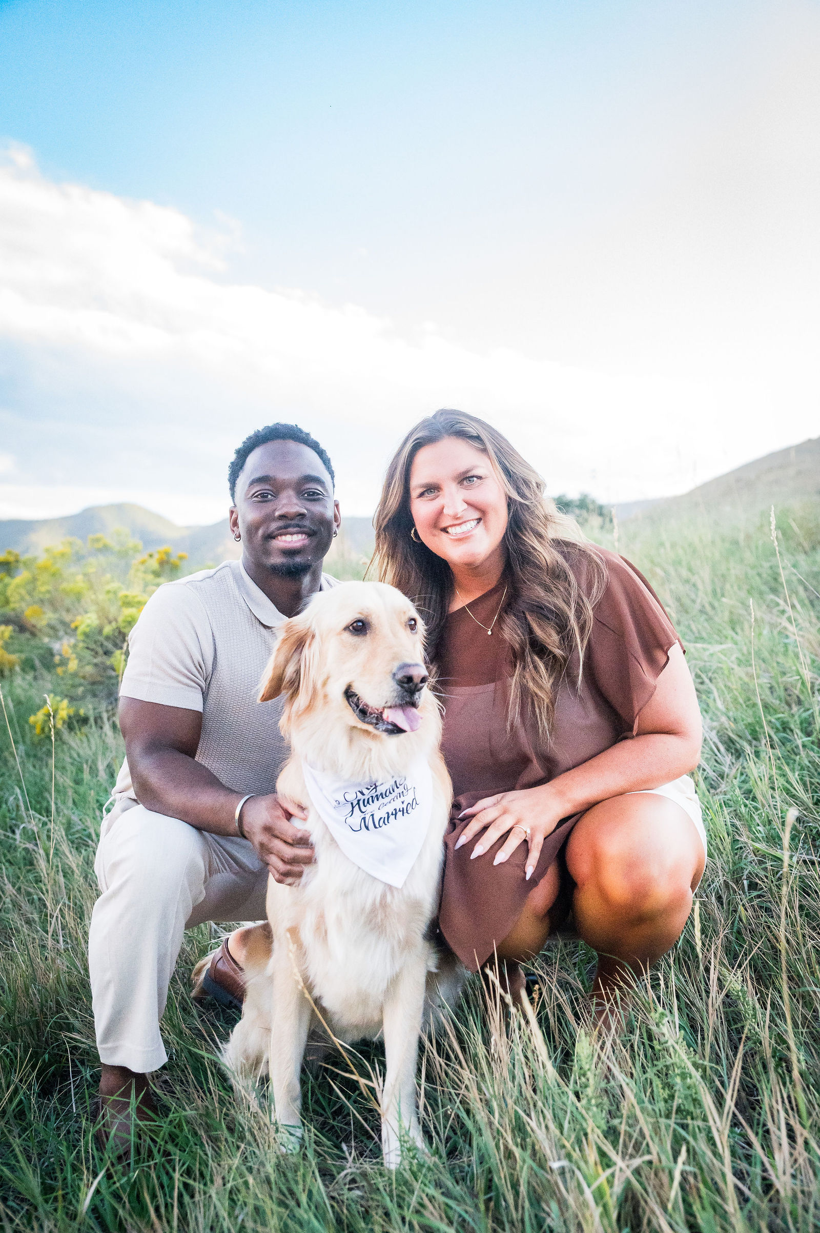 Engaged couple in cream and chocolate brown outfits with their golden retriever in a Colorado field