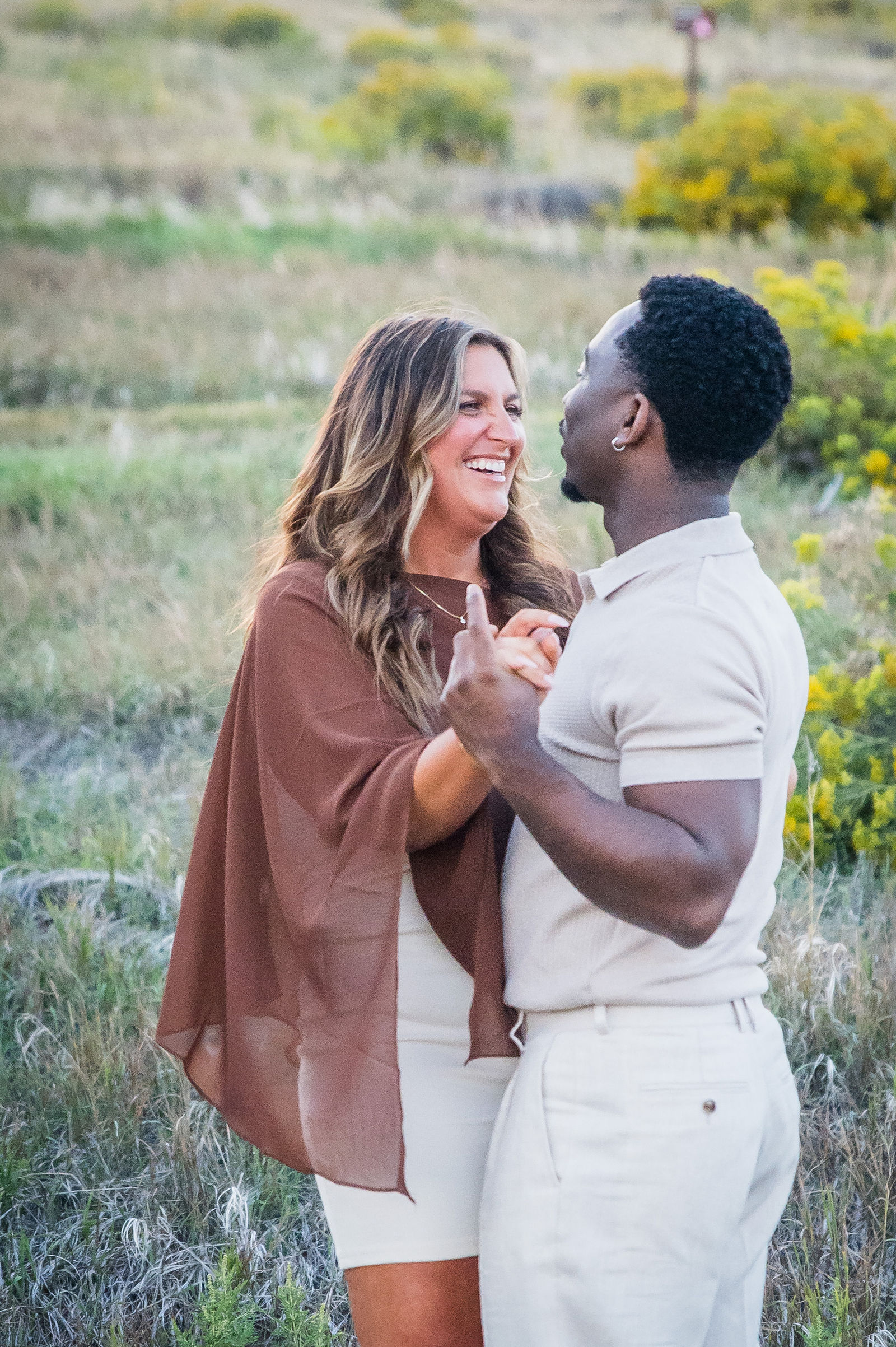 Bride to be wrapped in a brown shawl layered over a cream outfit during a fall engagement session