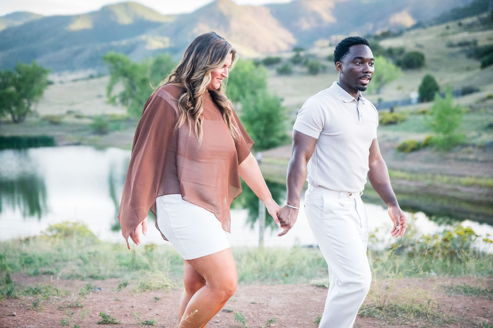 Engaged couple walking hand in hand, she is wearing a rust wrap layered over her outfit