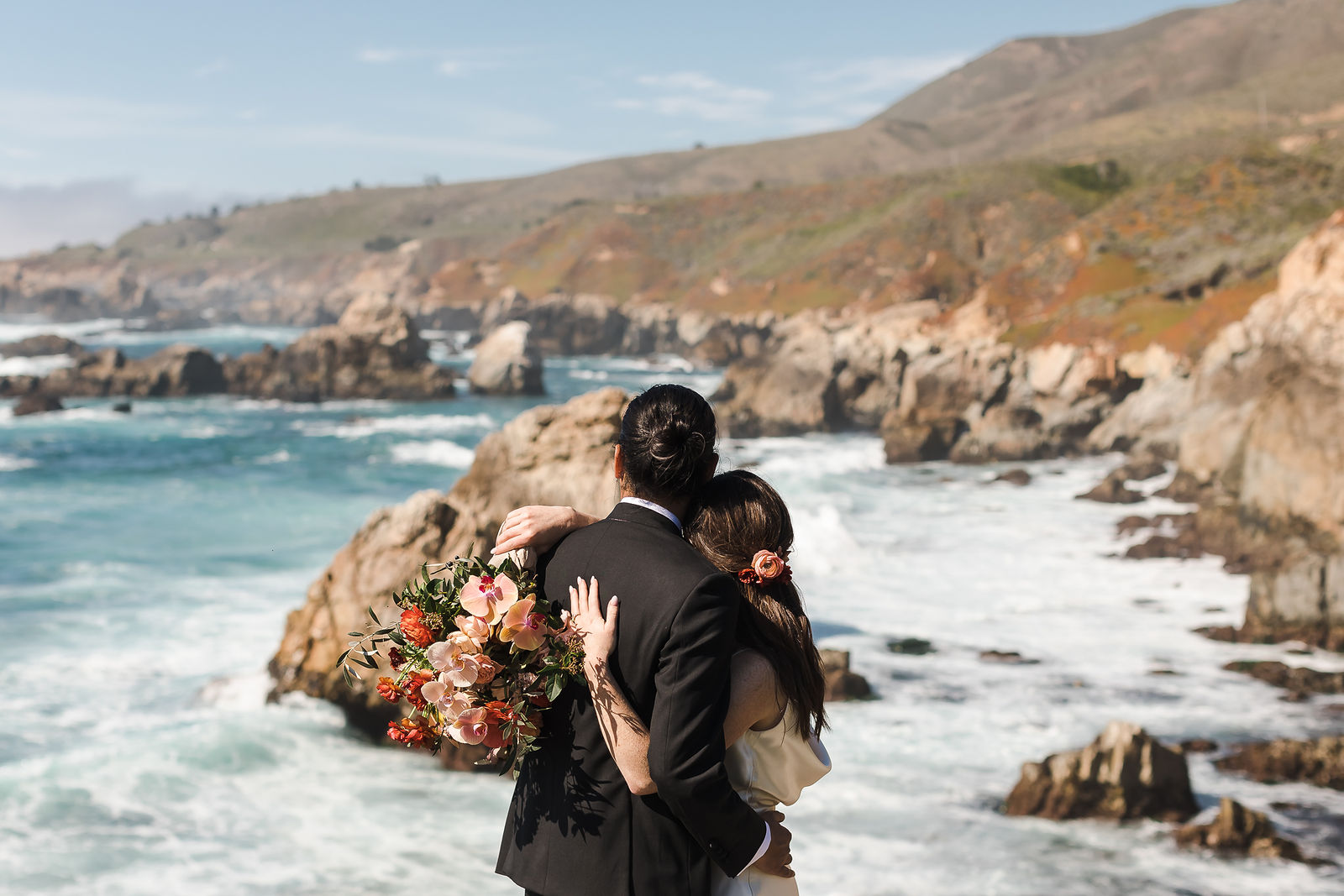 Couple embracing on the rocky Big Sur coastline during destination wedding portraits