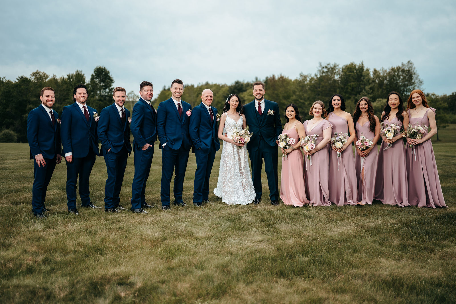Full wedding party posed on the lawn in front of the manor house at Dell-Lea