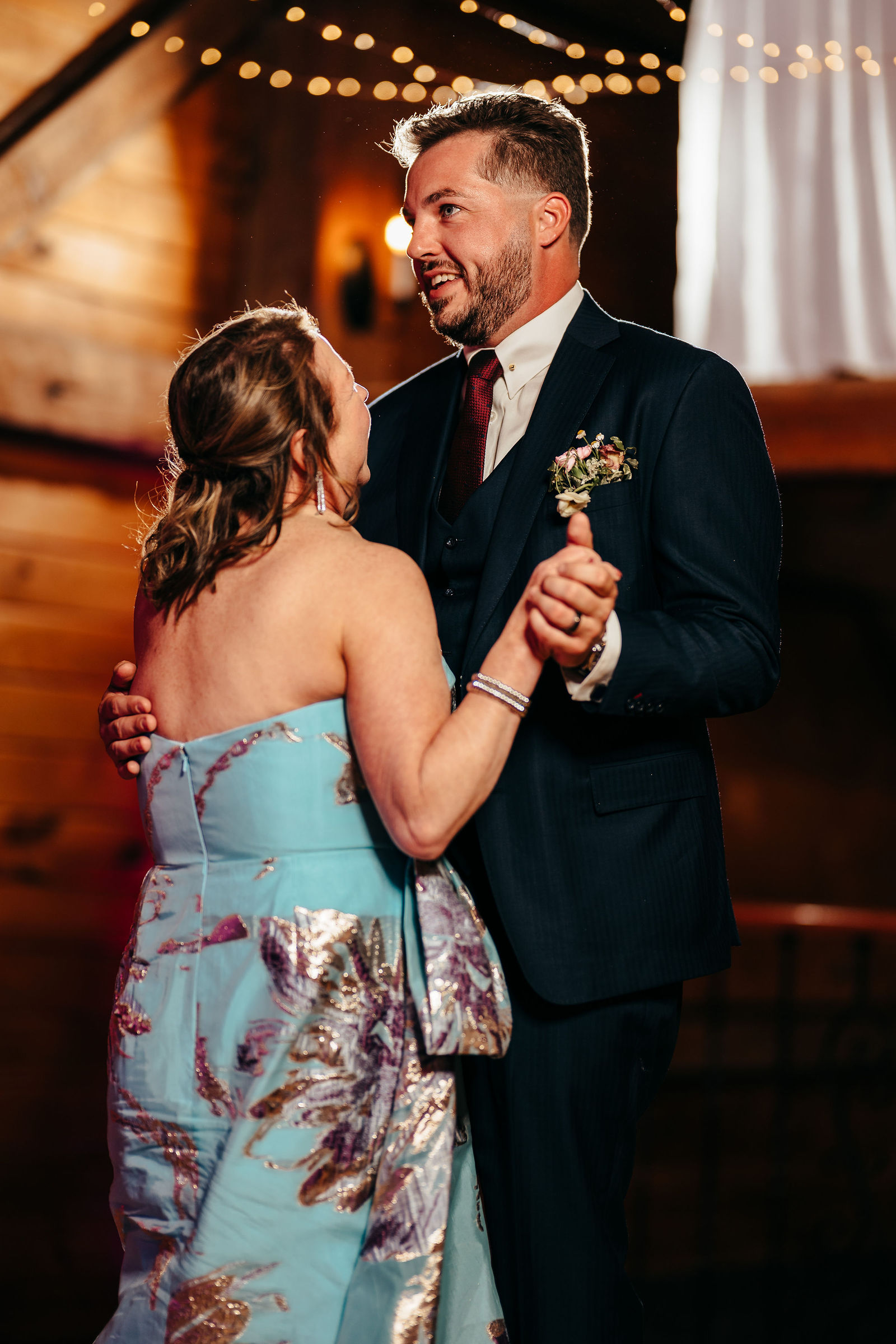 Groom sharing a mother-son dance in the barn reception hall with wood walls and string lights at Dell-Lea