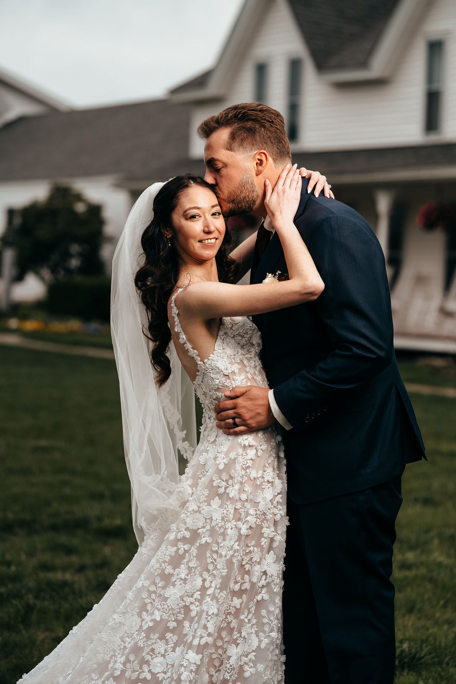 Groom kissing the bride's cheek on the lawn in front of the manor house and wraparound porch at Dell-Lea