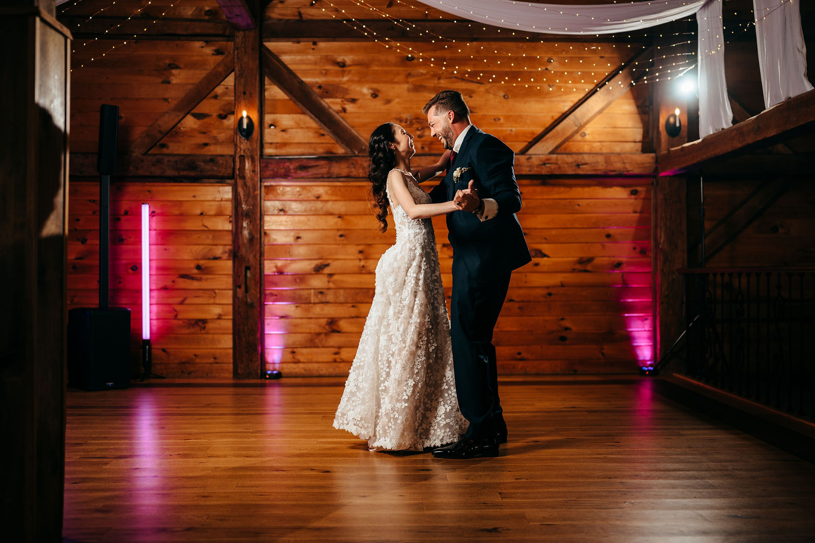 Bride and groom laughing during their first dance in the barn reception hall under string lights at Dell-Lea
