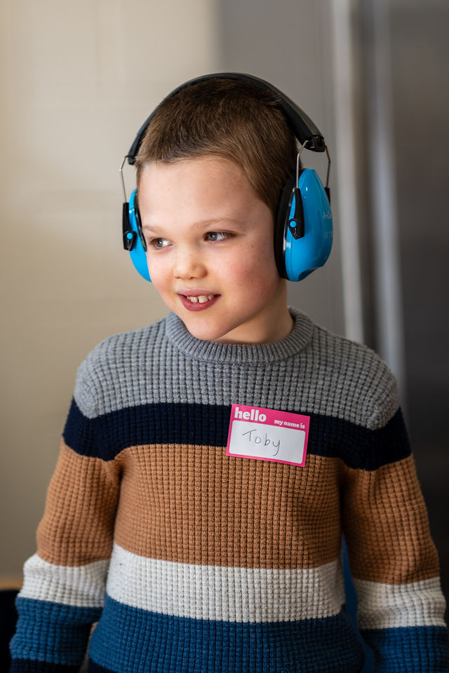 A child wearing blue ear defenders smiling in soft window light.