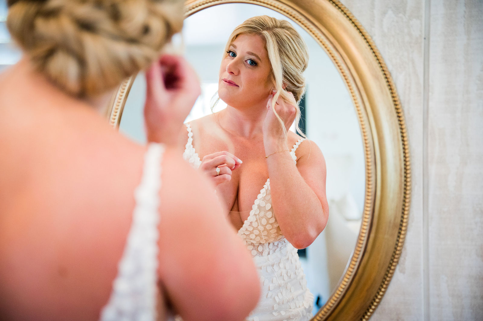 Bride putting on her earrings in the mirror before her Woodlands wedding