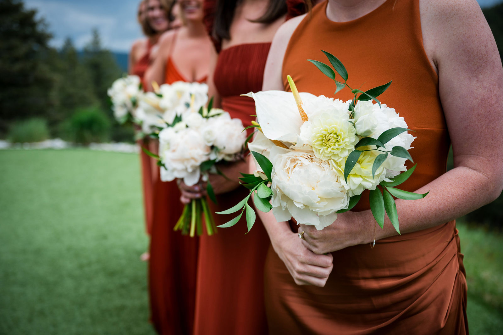 Bridesmaids holding white and orange bouquets at a Colorado wedding ceremony