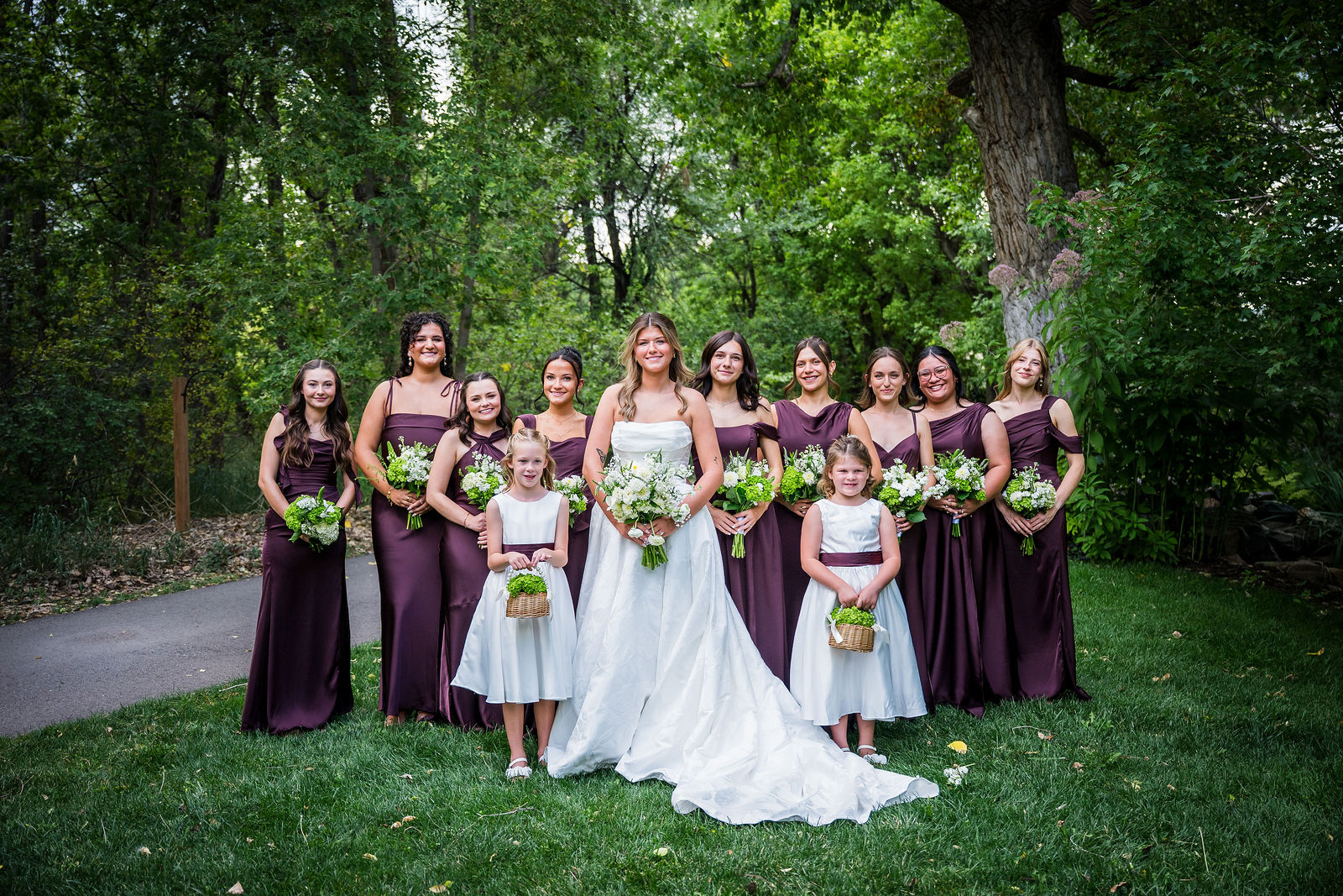Nine bridesmaids in deep plum dresses in the gardens