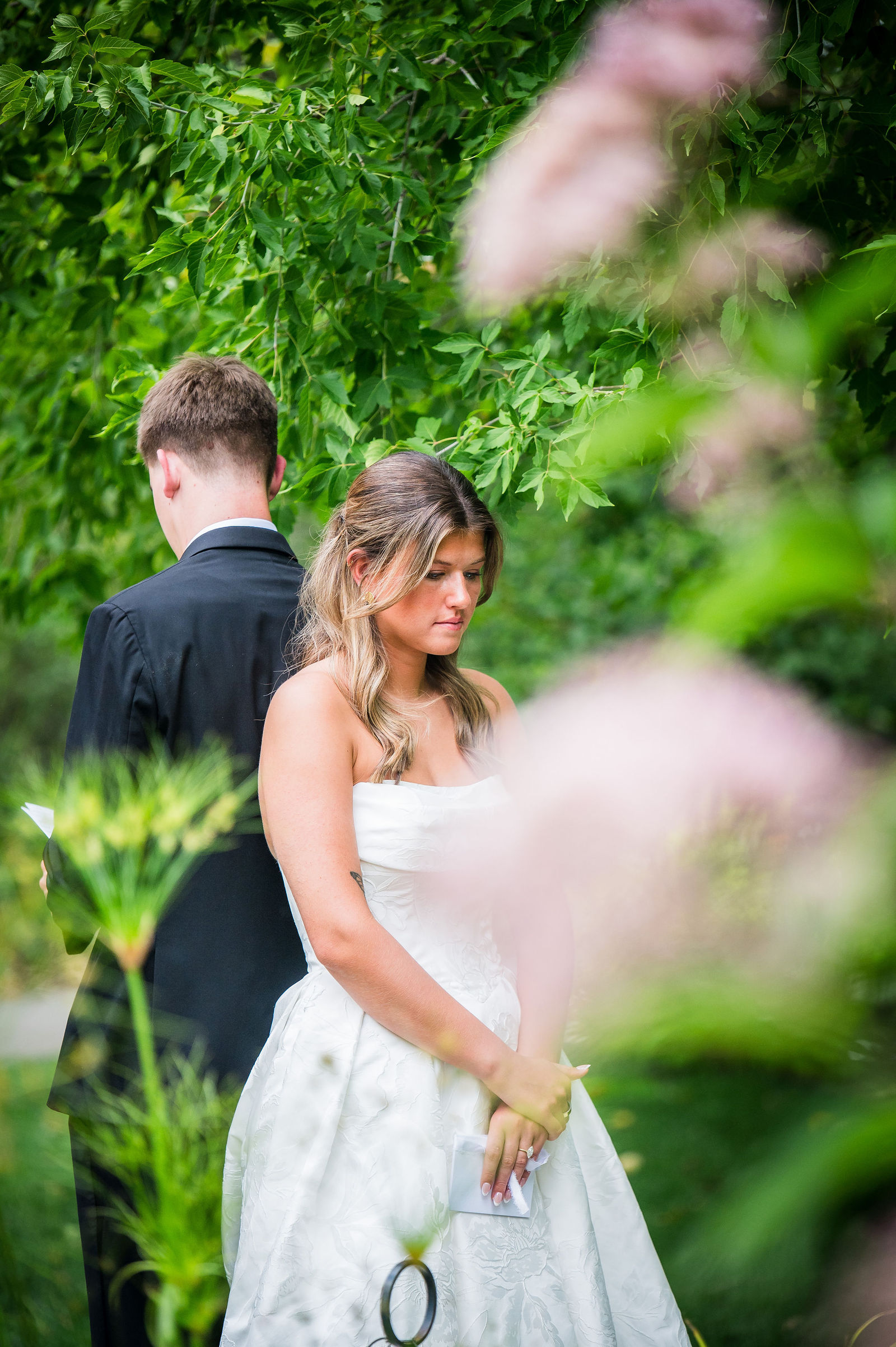 Bride and groom back to back among the blooms reading vows