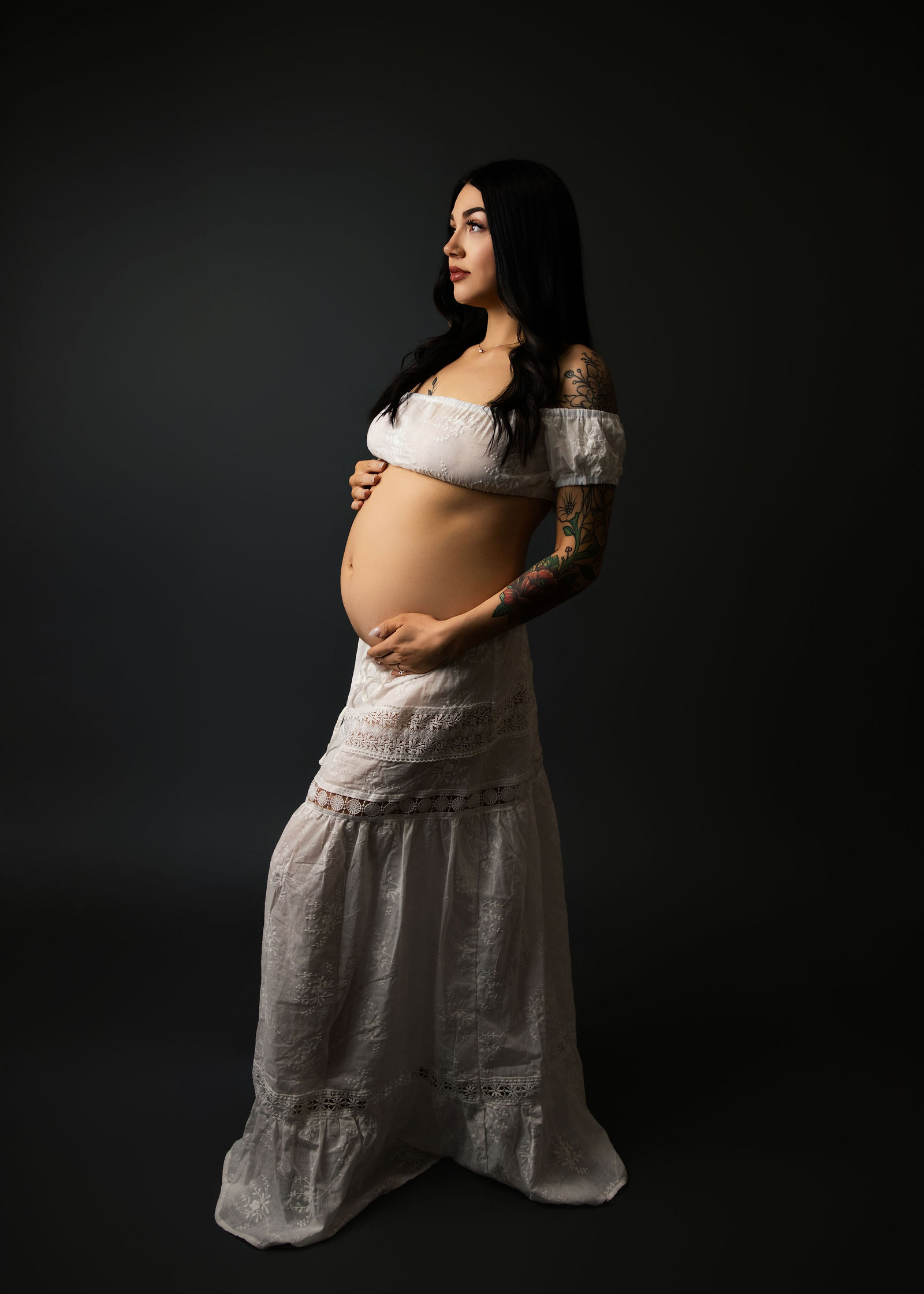 Pregnant woman in a flowing red gown posing against a dark studio backdrop